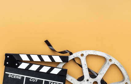 A cinema clapperboard, film canister, and reel of cinema film above a dark yellow background