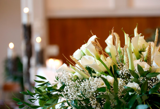 A close-up display of white funeral flowers set against the blurred interior of a church