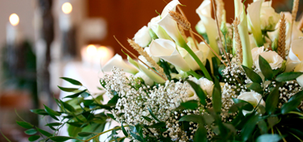 A display of white funeral flowers set against the blurred interior of a church